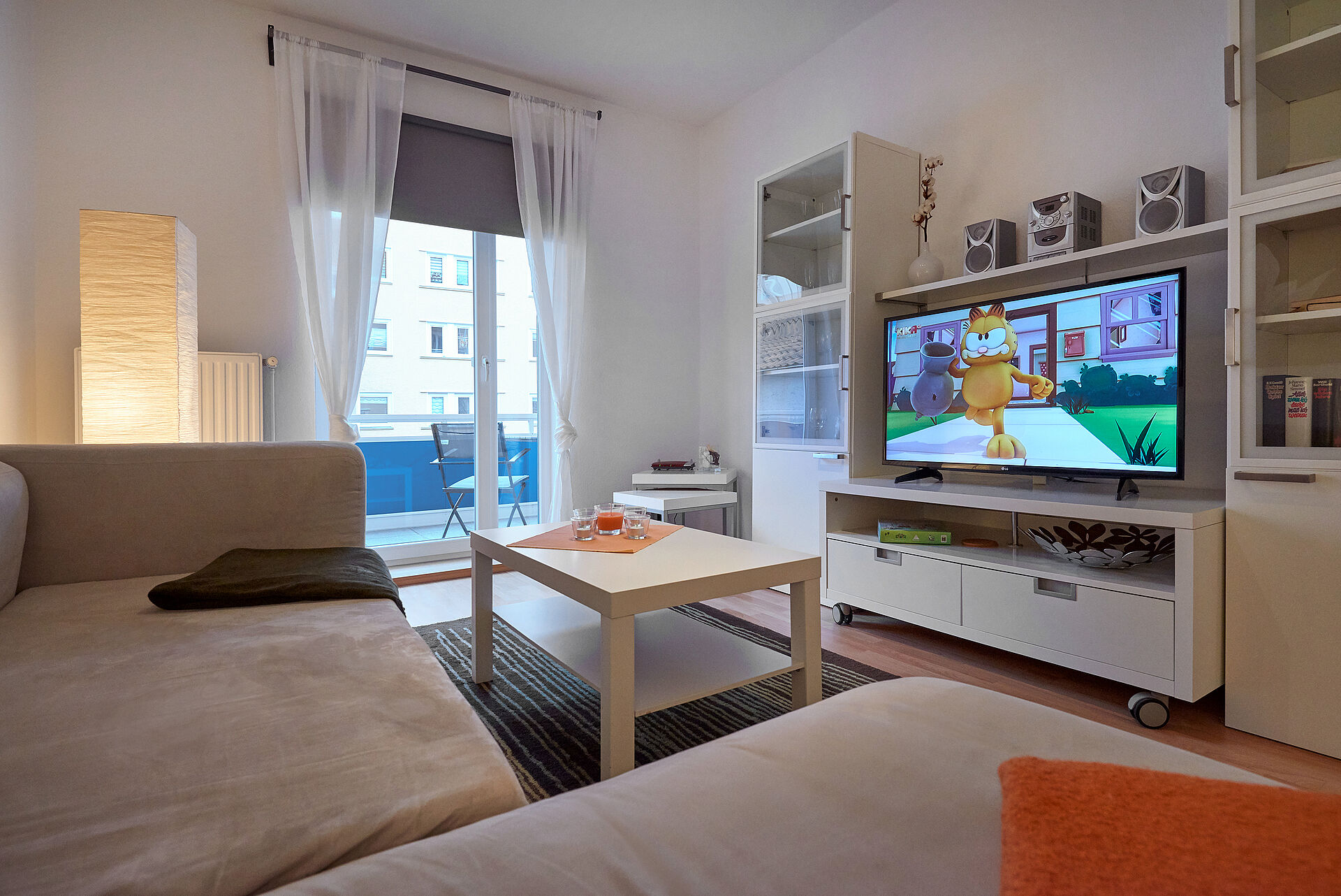 Wohnzimmer mit bodentiefen Fenstern, davor eine große Couch, der Blick fällt auf den Wohnzimmerschrank mit TV