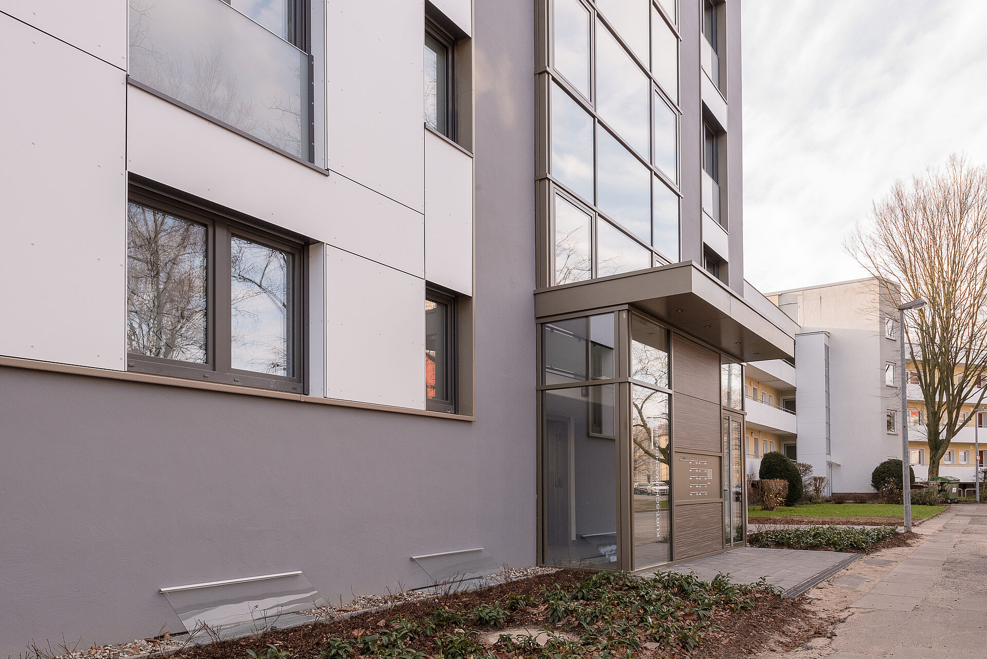 Mehrfamilienhaus mit steingrauer Fassade und weiß abgesetzten Farbflächen