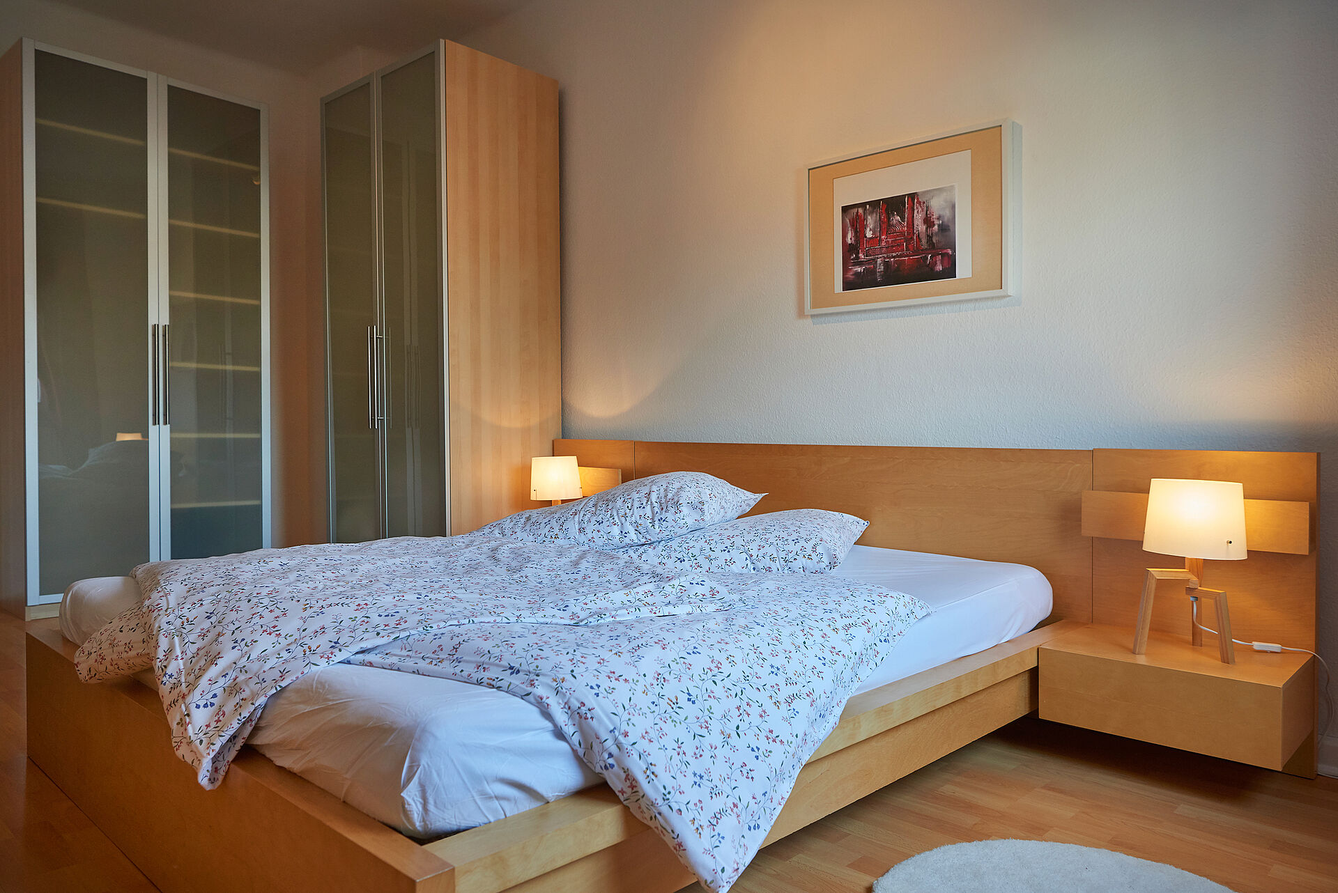 Schlafzimmer mit einem Doppelbett aus Holz, auf dem Nachttisch leuchten elegante Lampen