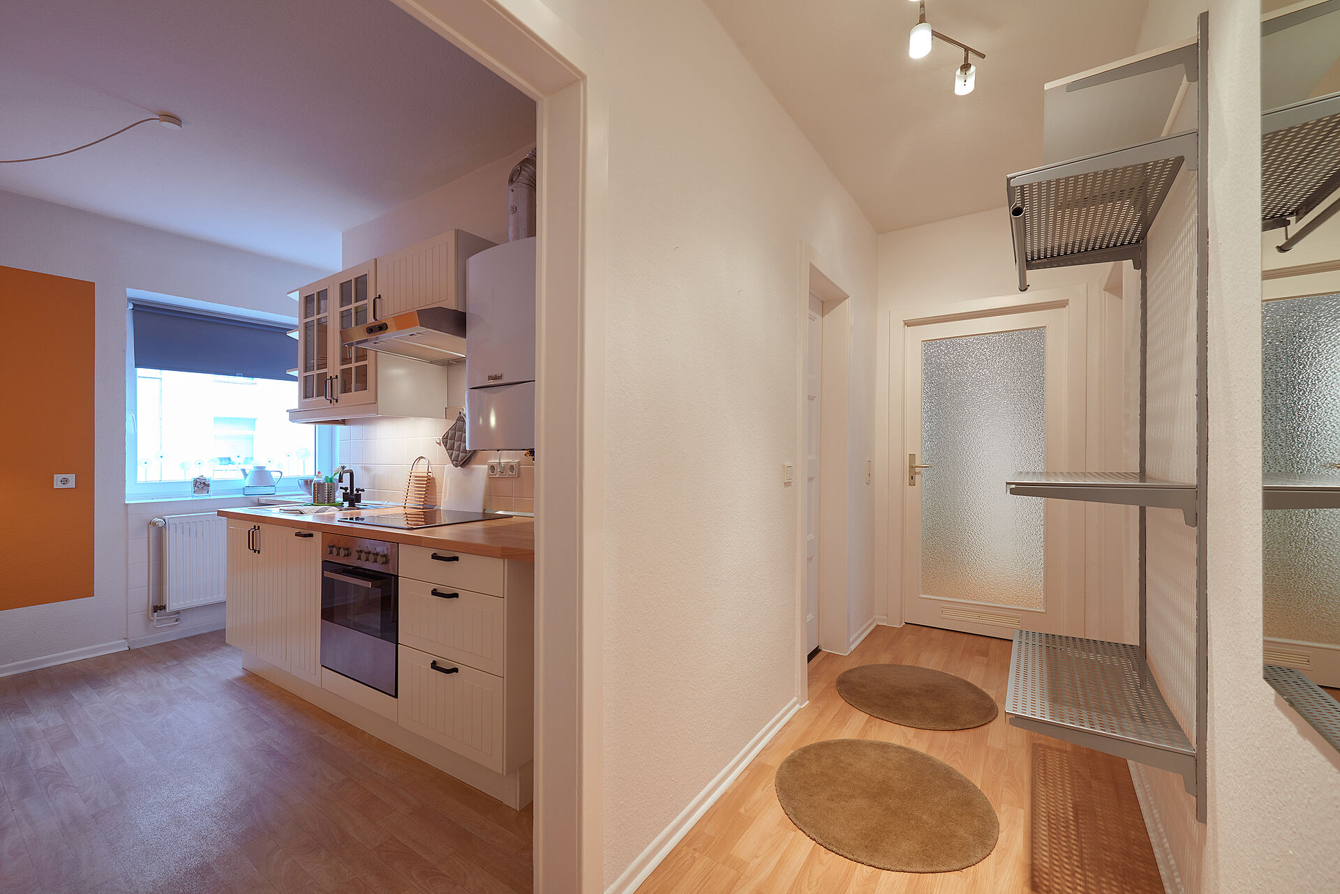 Blick auf dem Wohnungsflur mit Regal und kleinen runden Teppichen Richtung Küche