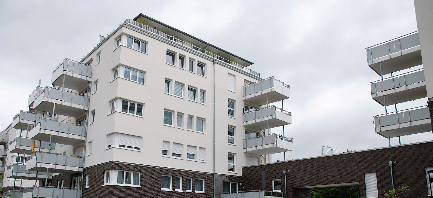 Mehrfamilienhaus mit Klinkersockel, heller Fassade und großen Balkonen