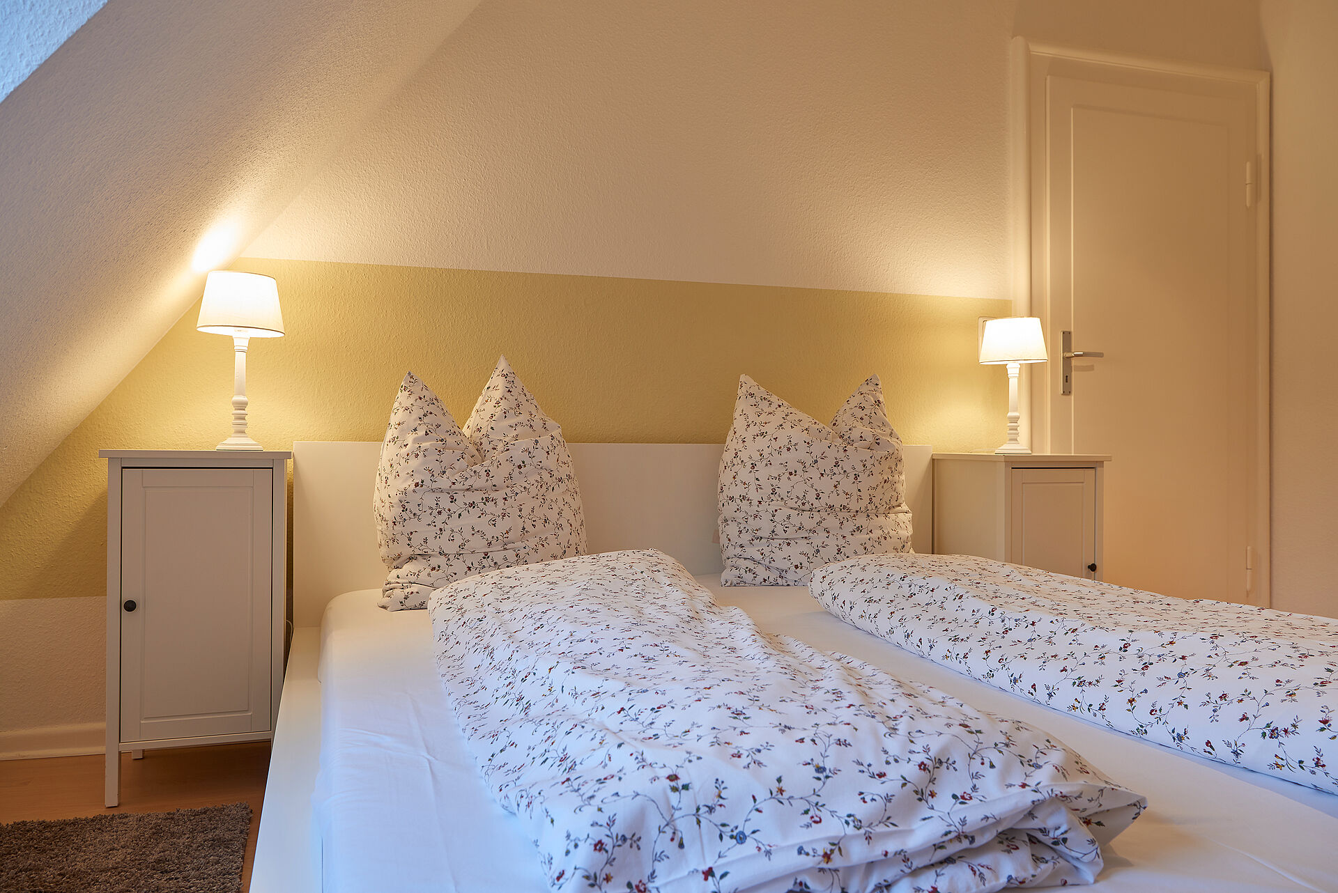 Schlafzimmer mit heller Bettwäsche und zwei Nachtschränken mit kleinen weißen Lampen