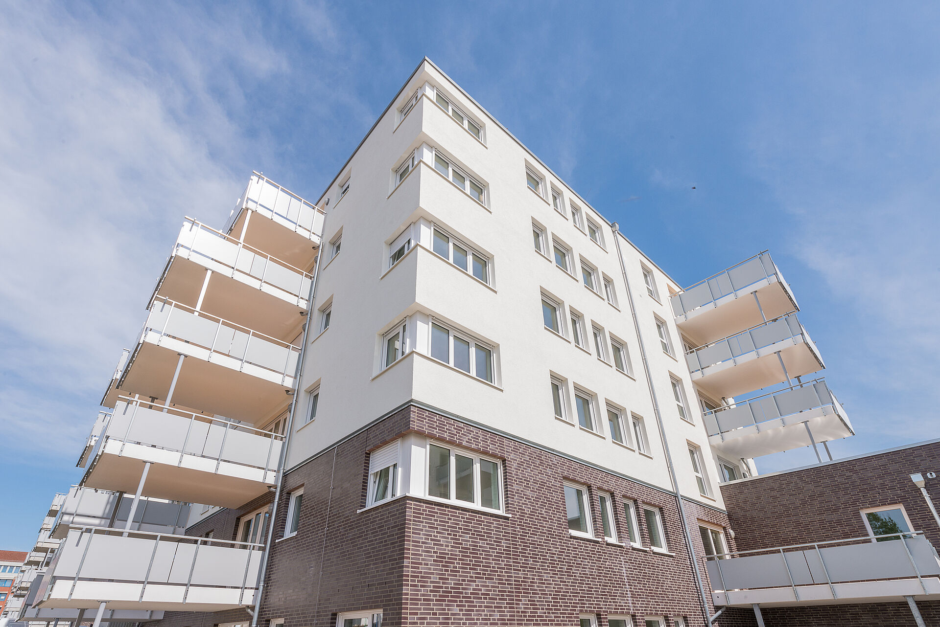Mehrfamilienhaus mit Klinkersockel, heller Fassade, Fenstern über Eck und großen Balkonen
