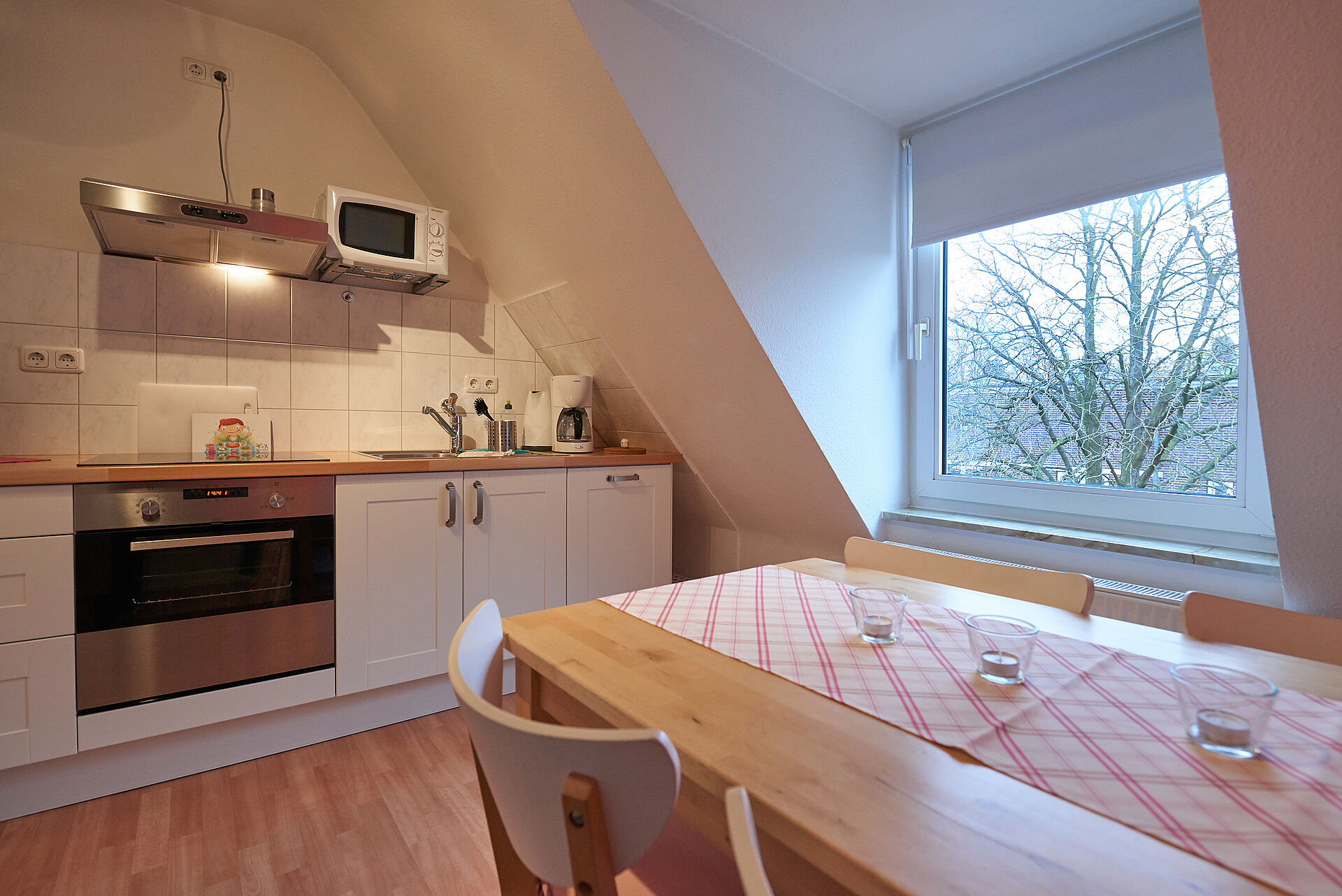 Küche mit Dachschräge, weiße Küchenschränke, eine Mikrowelle und ein Küchentisch mit Stühlen