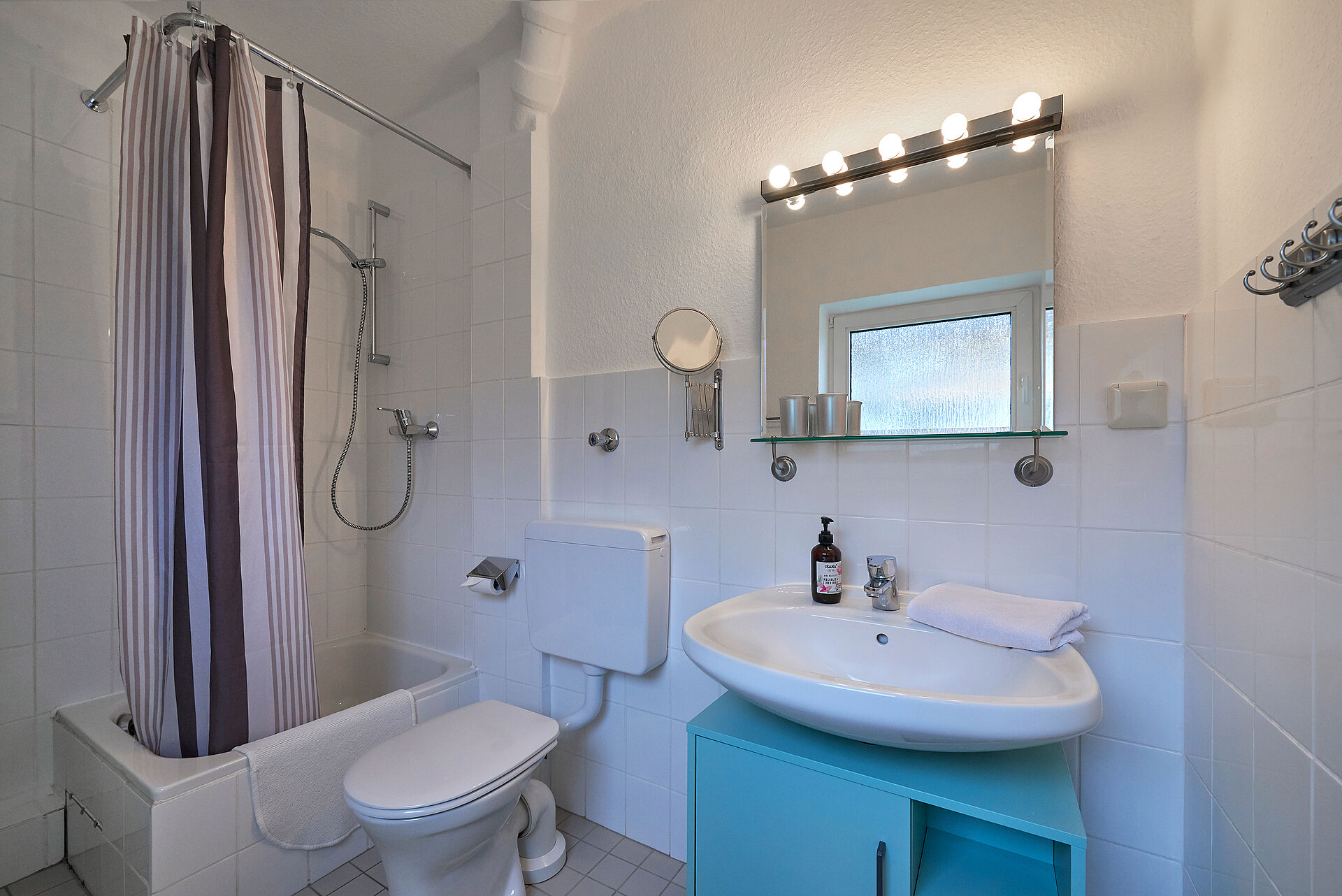 Helles weißes Badezimmer mit Dusche und Duschvorhang, der Waschbeckenunterschrank ist hellblau