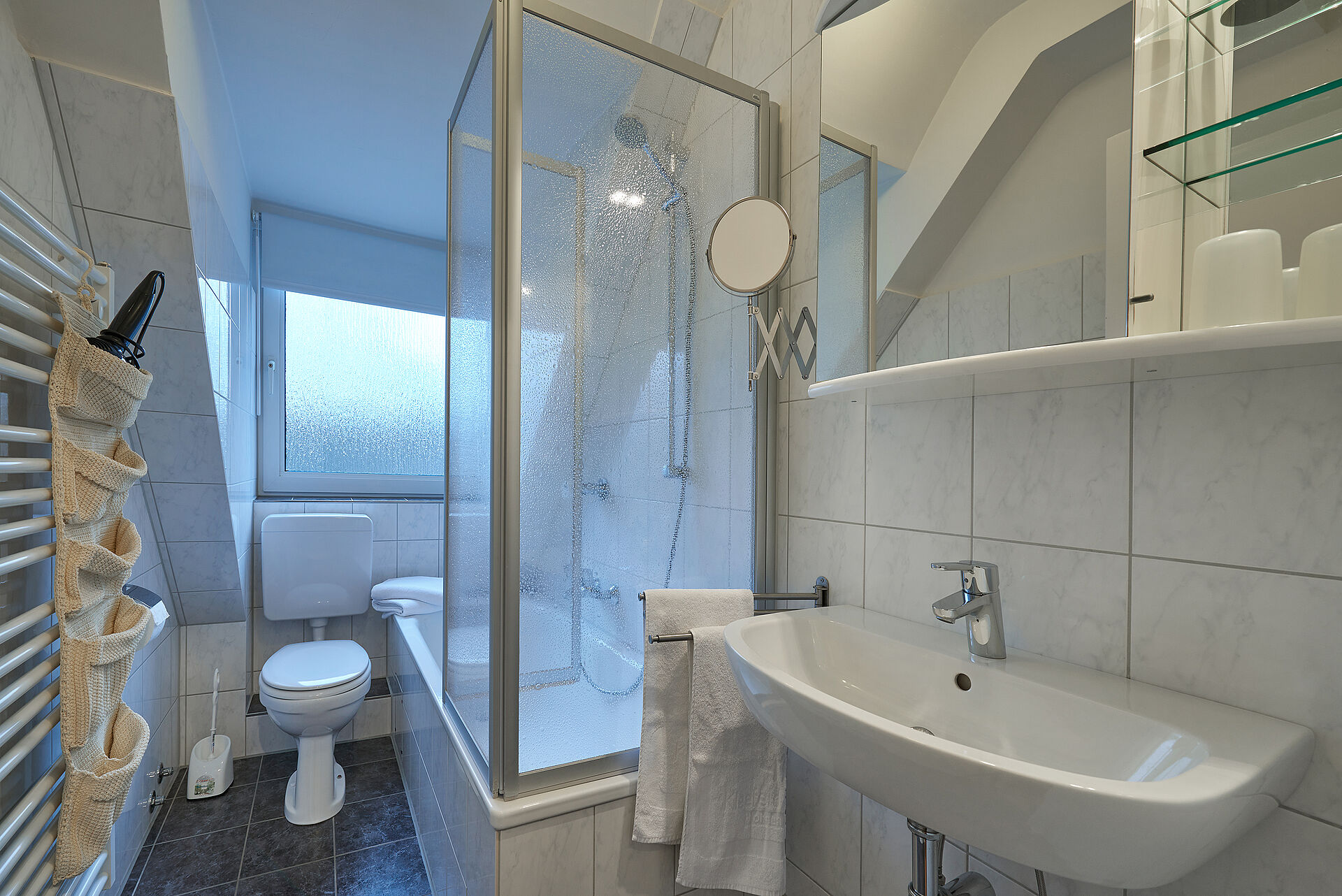 Hell gefließtes Badezimmer mit Dusche und Duschkabine, über dem Waschbecken hängt ein Spiegelschrank
