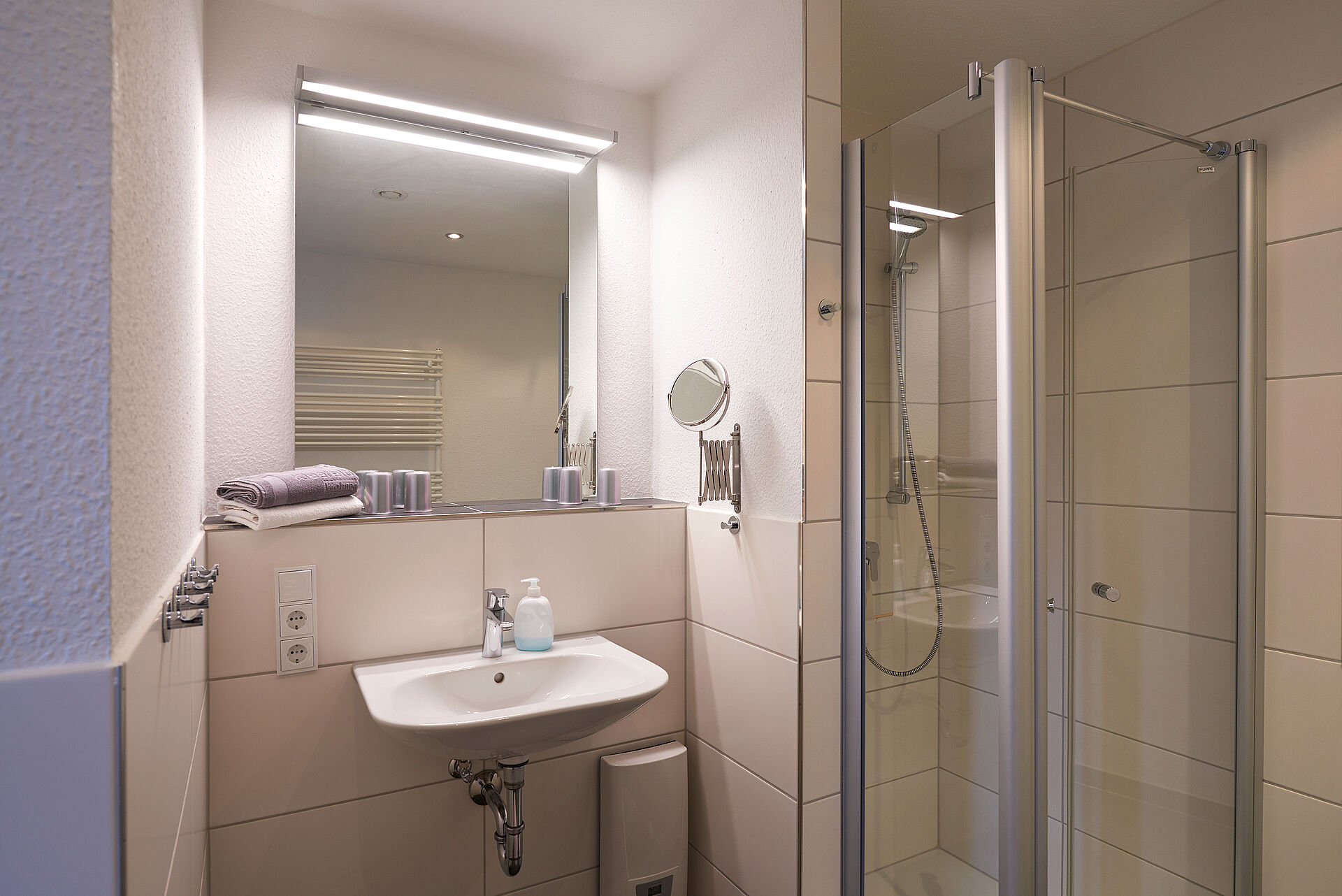 Badezimmer mit beleuchtetem Spiegel, einem Kosmetikspiegel und einer Dusche mit Duschkabine